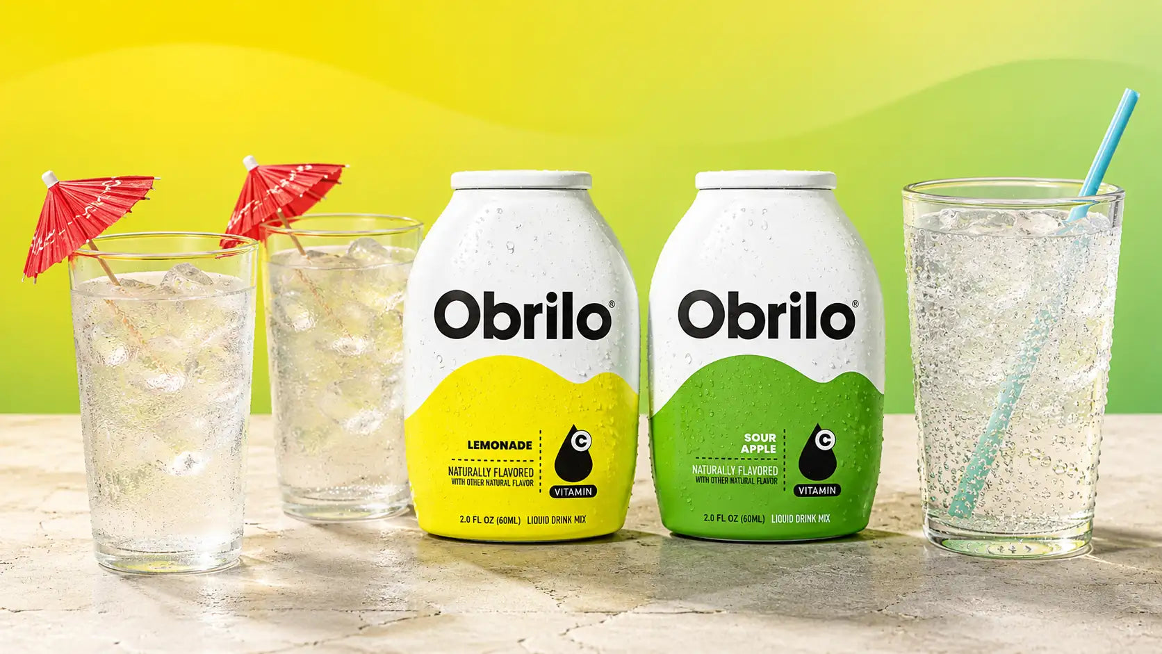 Two white obrilo soda bottles, one with a yellow label for lemonade and the other with a green label for sour apple.