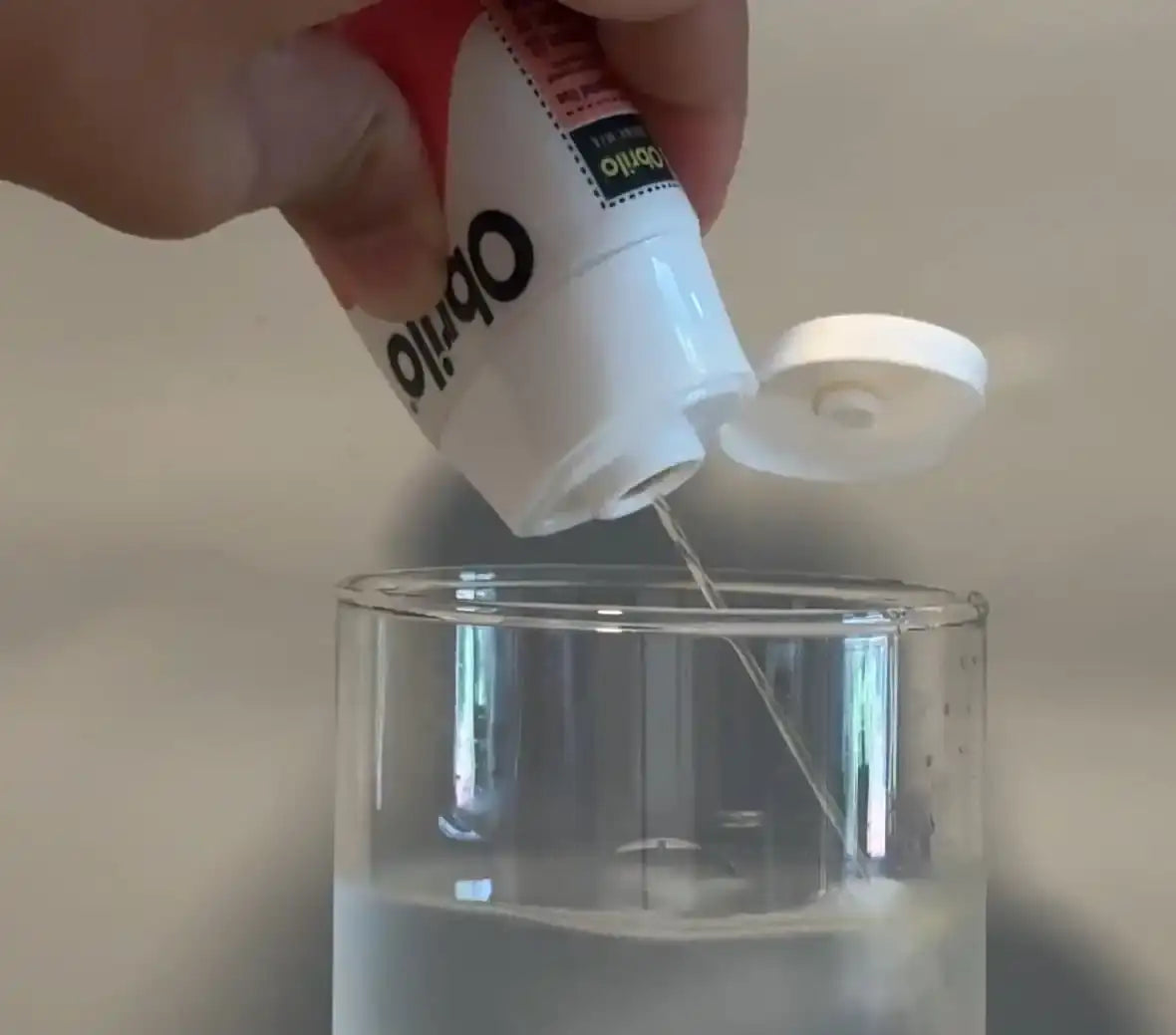 Liquid being poured from a squeeze bottle into a glass of water.