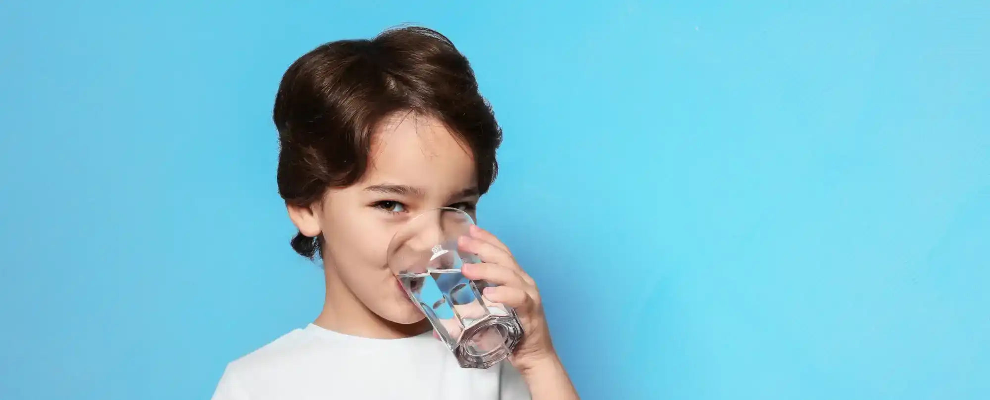 A young boy with brown hair drinking from a clear glass of water.